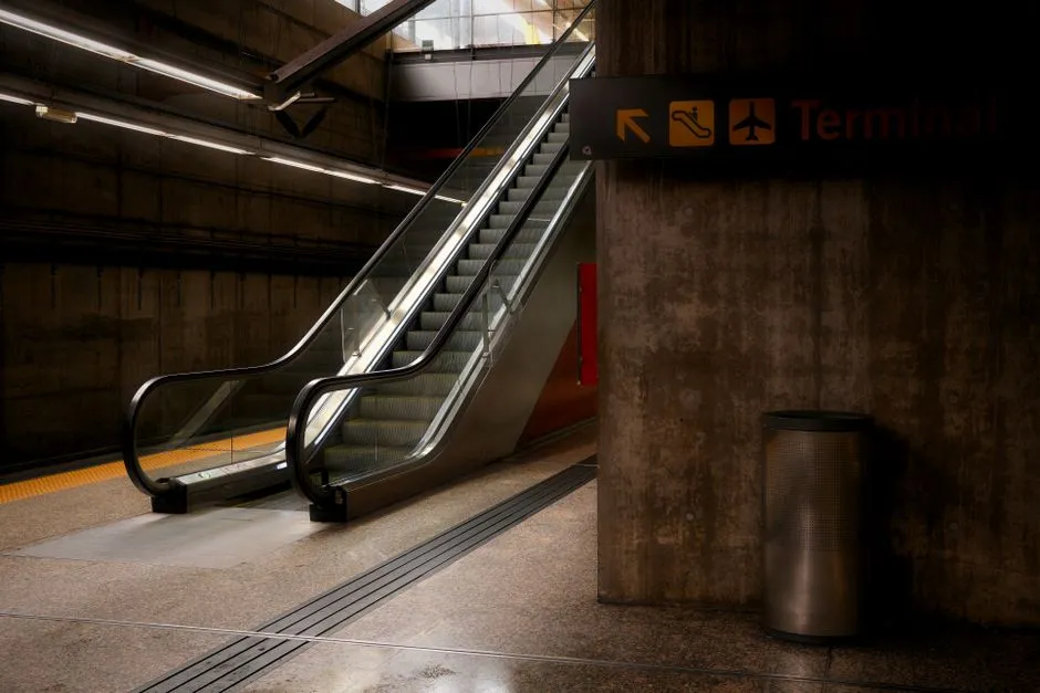 Empty airport terminal concourse with escalators and overhead signage